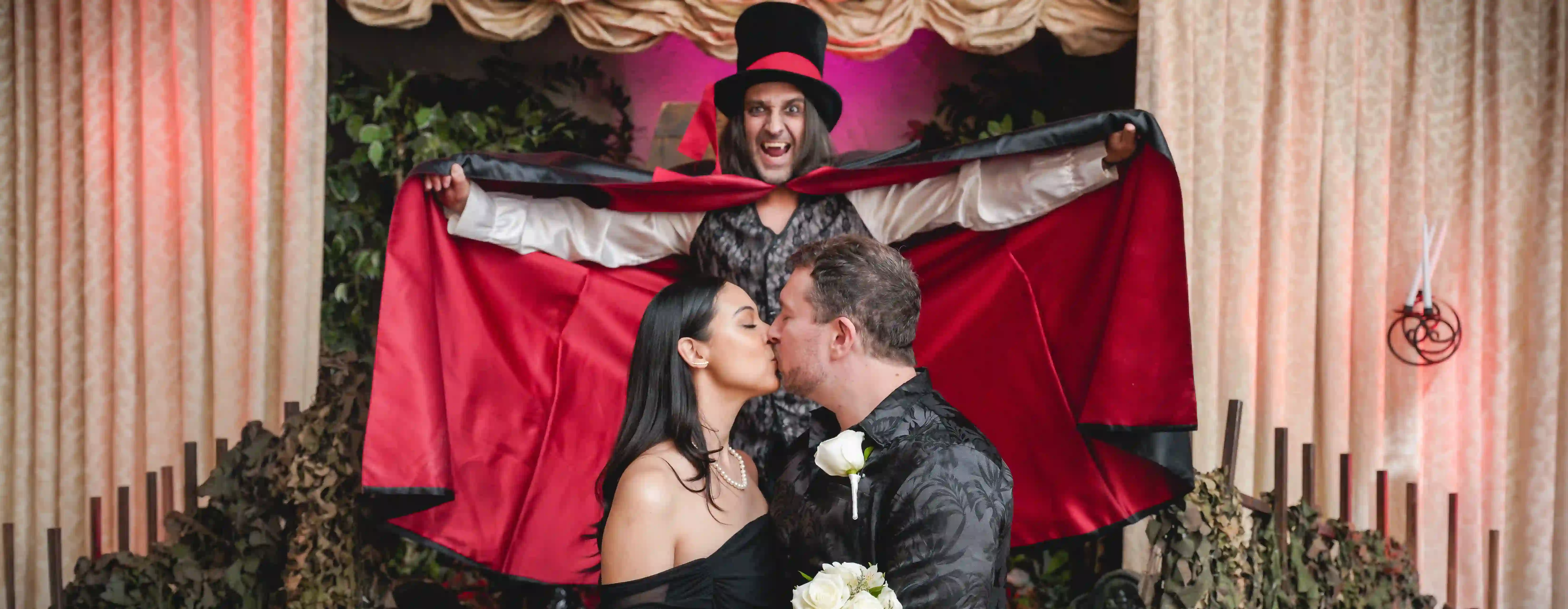 Dracula impersonator spreads his cape as the couple kisses at their wedding