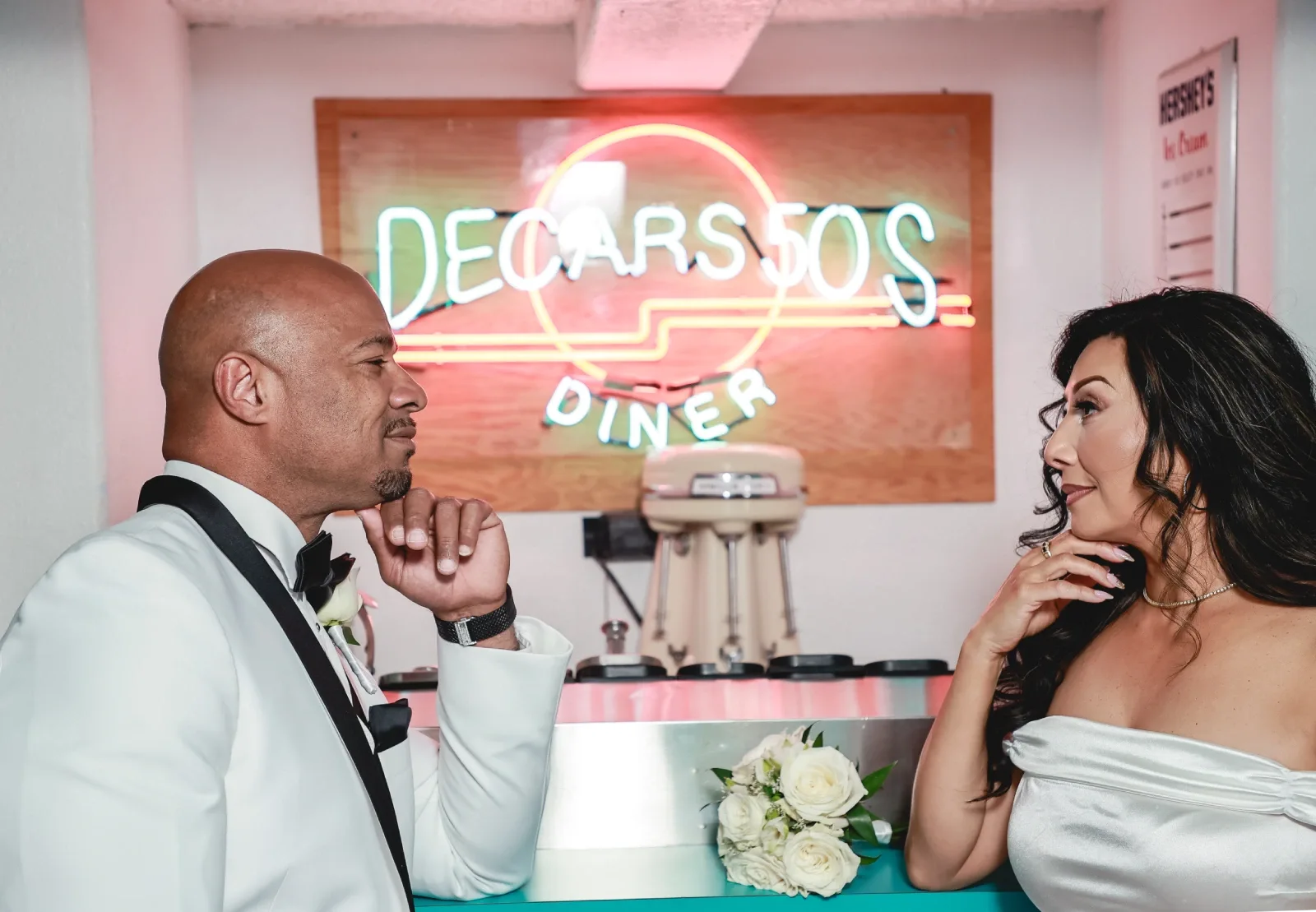 Bride and groom gazing at each other at a retro 50s diner counter with a neon sign at a Las Vegas wedding venue.