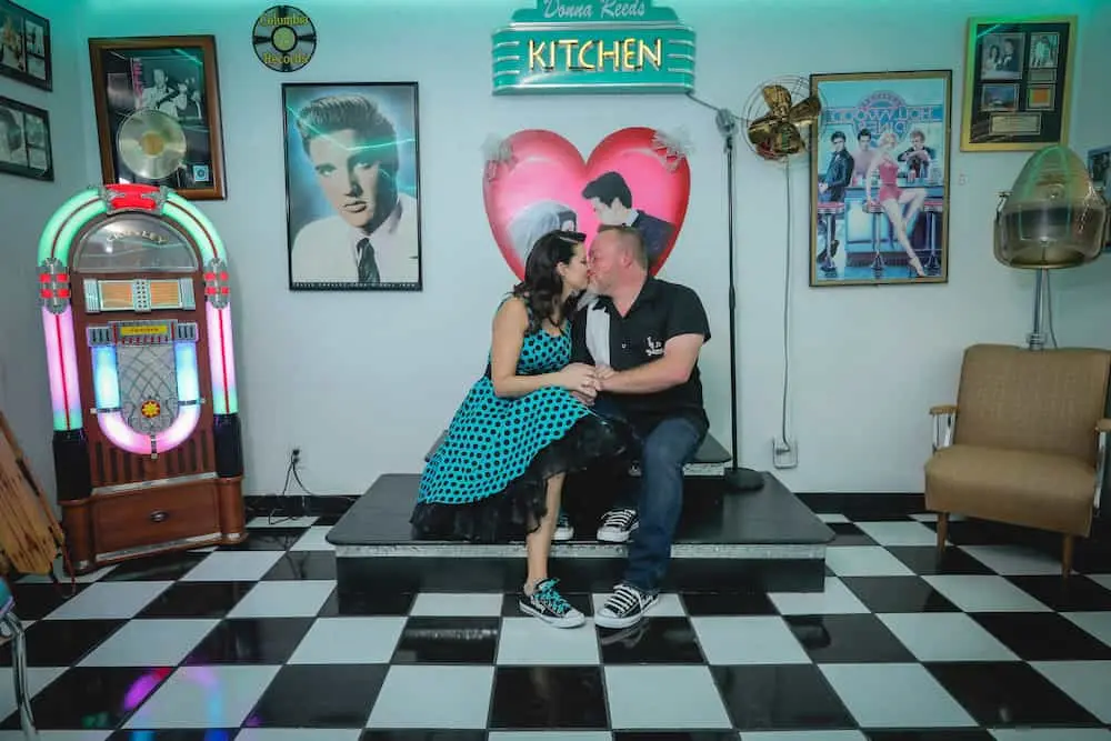 Couple in polka dots kissing on checkered floor next to jukebox in retro diner at Las Vegas wedding chapel