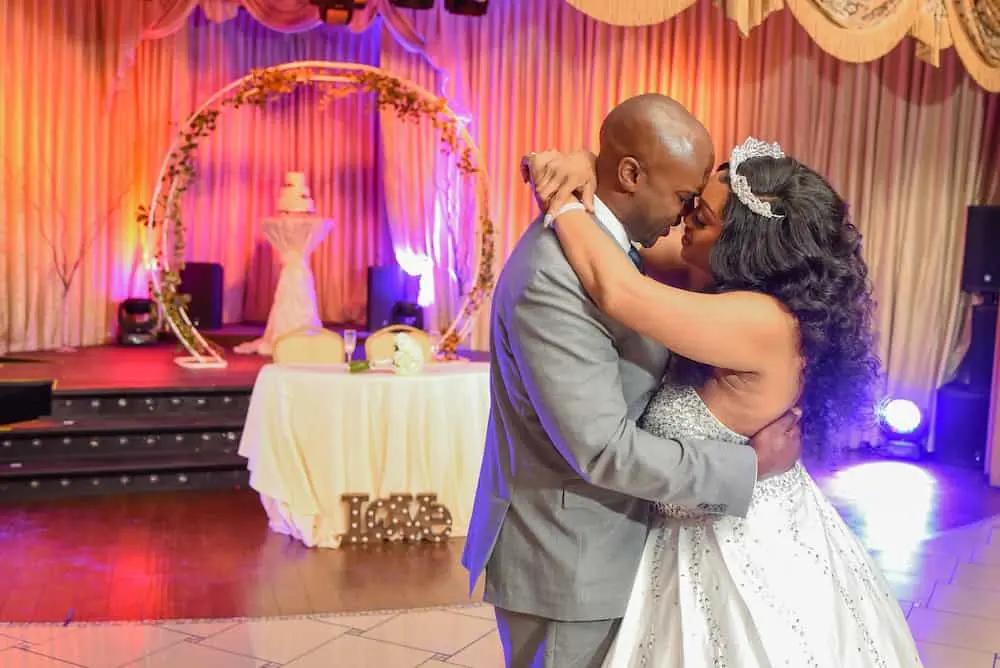 Couple sharing first dance with floral arch and wedding cake under colorful lights at Vegas Event Center