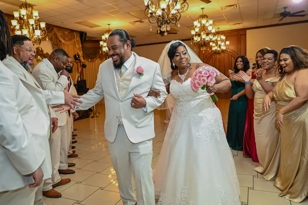 Bride and groom walking through cheering wedding party under chandeliers at Vegas Event Center