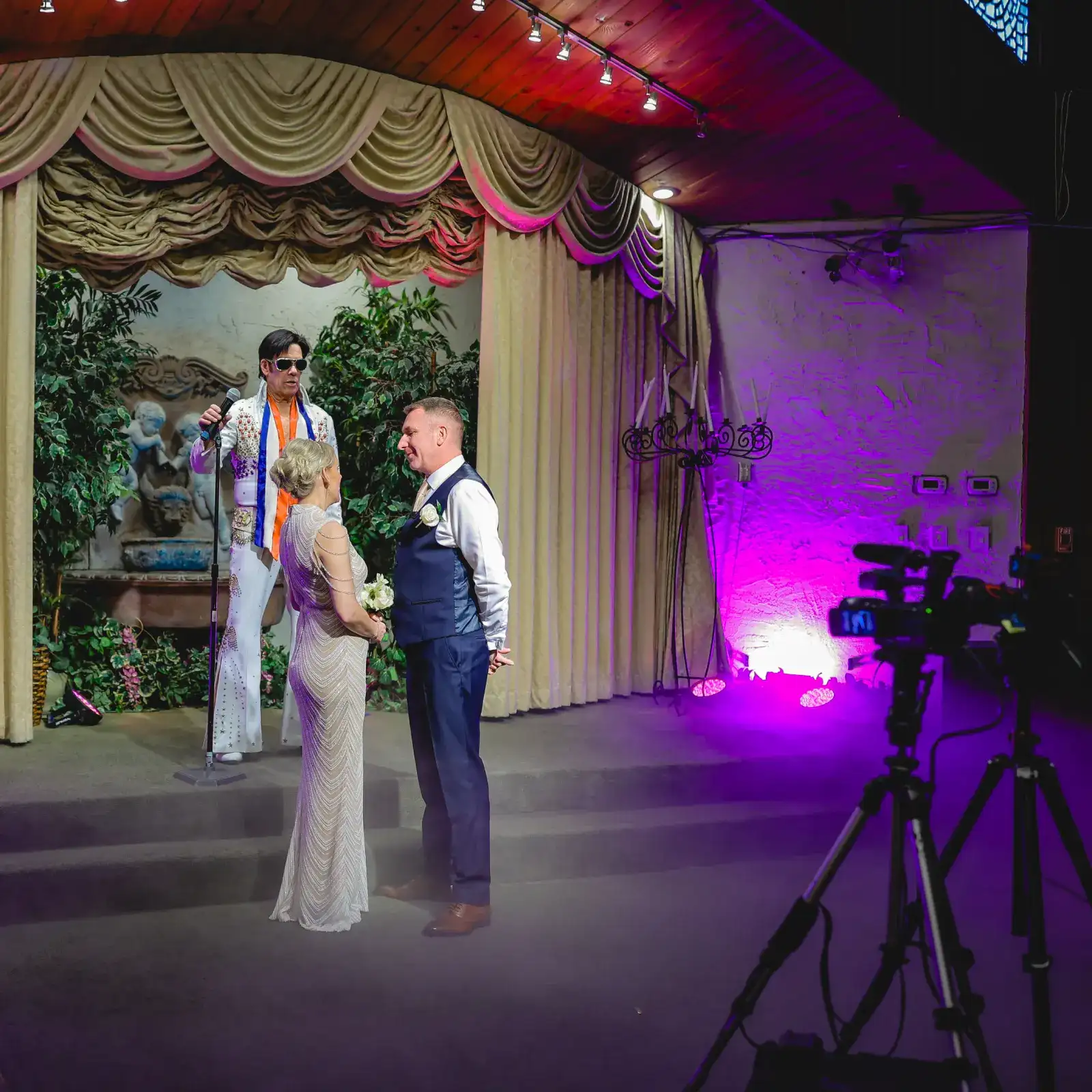 wedding couple with Elvis officiant on stage, filmed by a camera