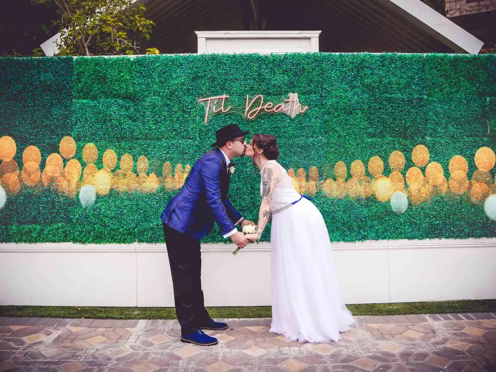 Couple kissing in front of greenery wall with til death neon sign at a Las Vegas wedding chapel