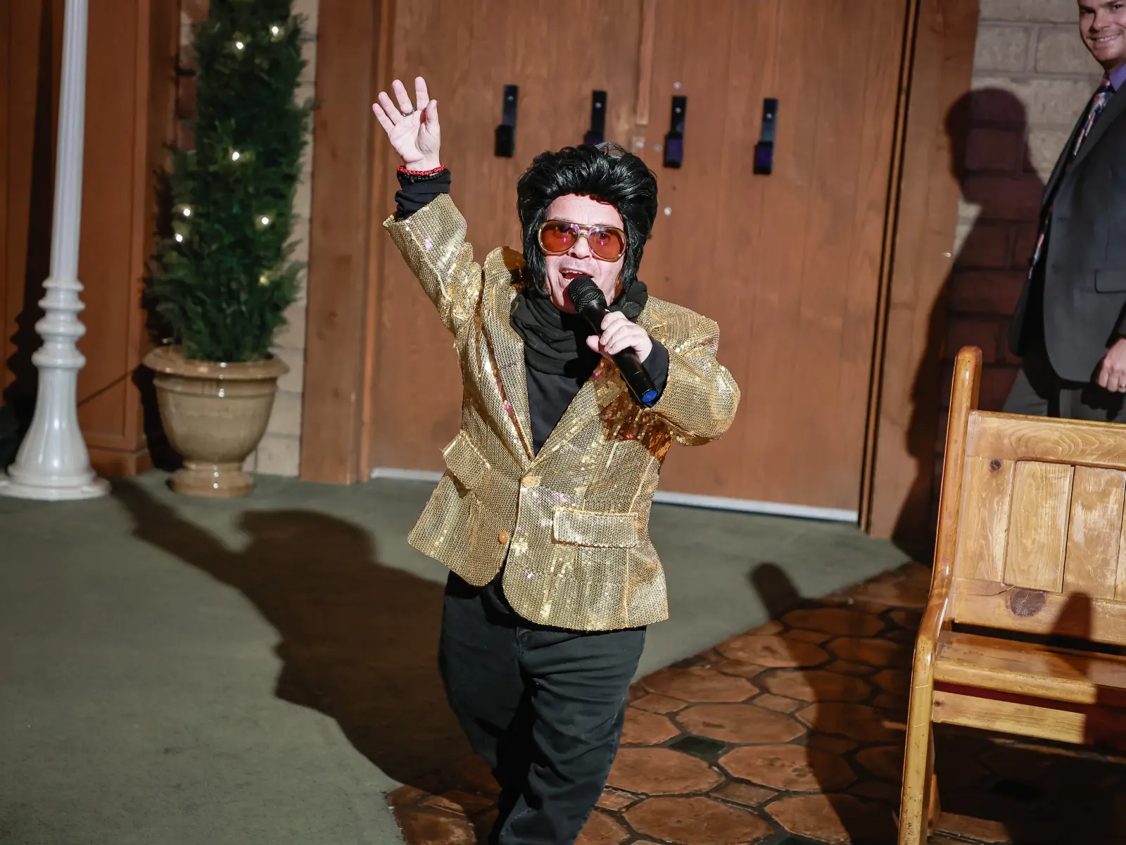 Energetic Elvis impersonator singing and entertaining wedding guests in Las Vegas chapel aisle wearing gold sequin jacket and sunglasses