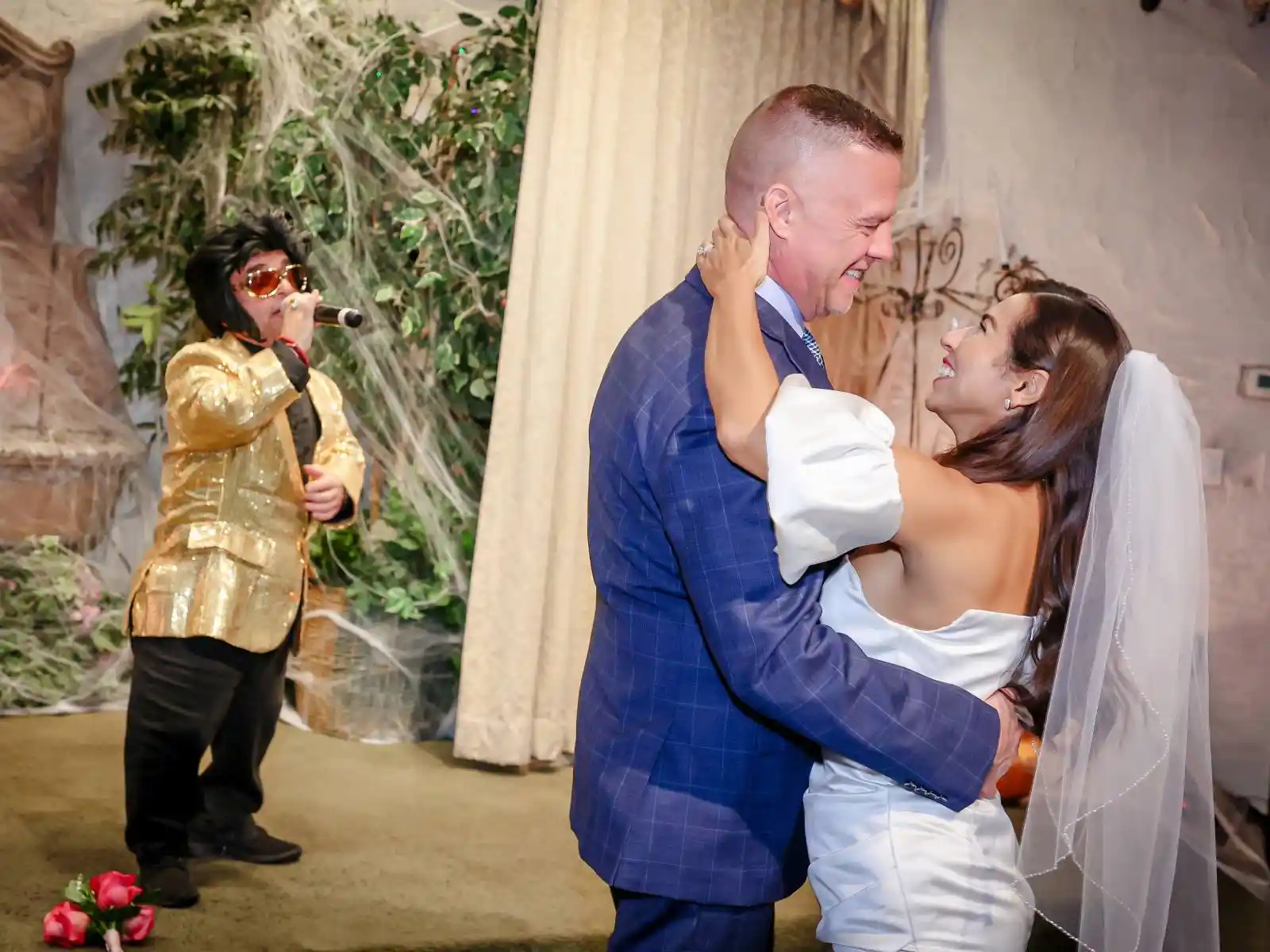 Couple sharing a romantic dip dance while mini Elvis impersonator in gold jacket serenades them at a Las Vegas wedding