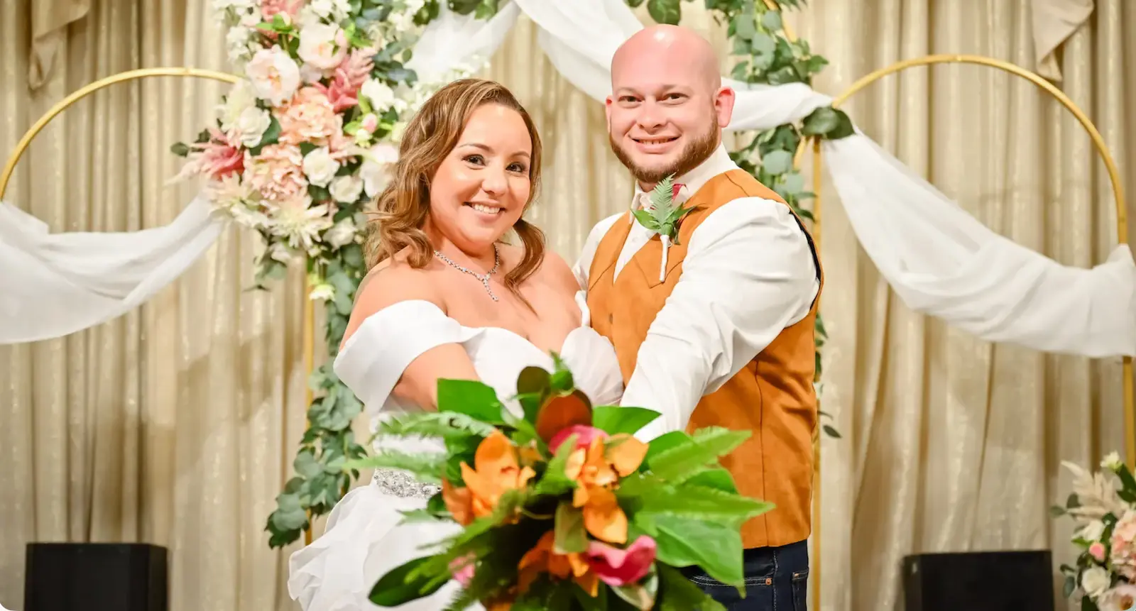 Couple posing with tropical bouquet under a greenery and floral arch at a Las Vegas wedding reception