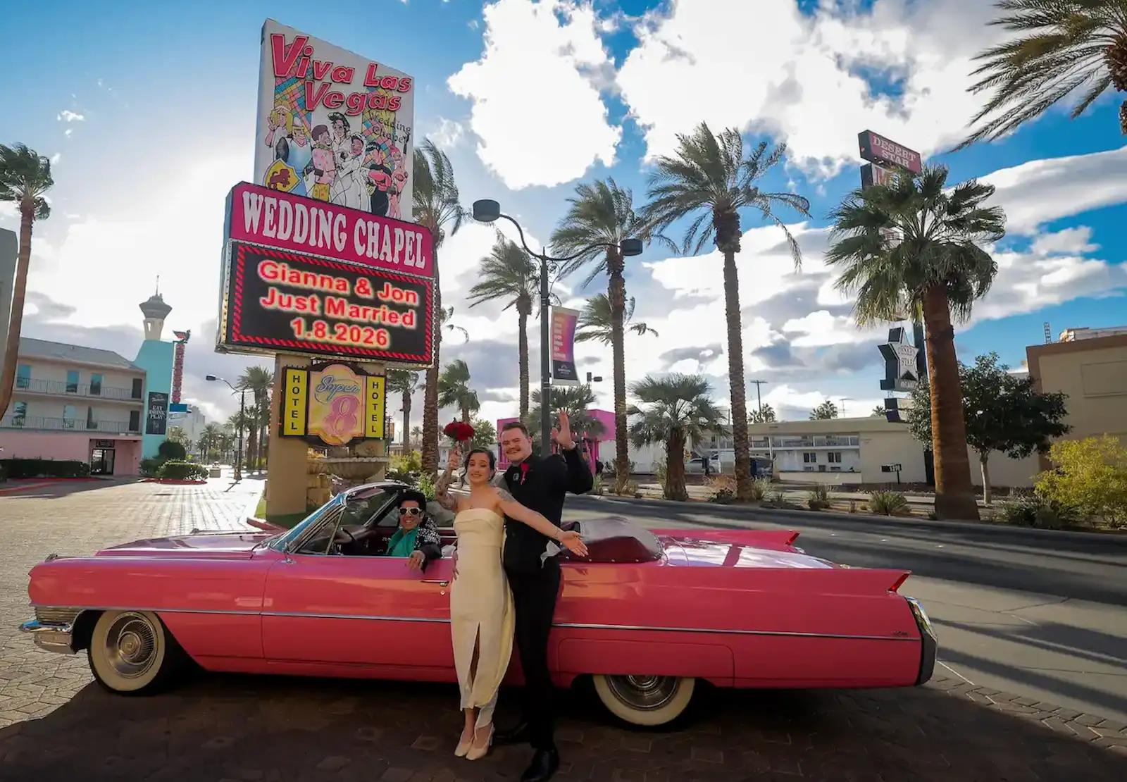 Just married couple posing with a pink Cadillac and Little Elvis in front of the Viva Las Vegas Wedding Chapel sign