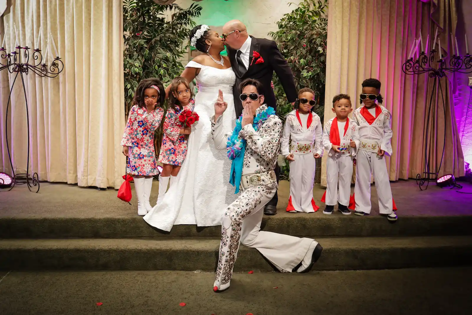Bride and groom kissing at Las Vegas Elvis wedding ceremony with Elvis officiant and children in Elvis costumes