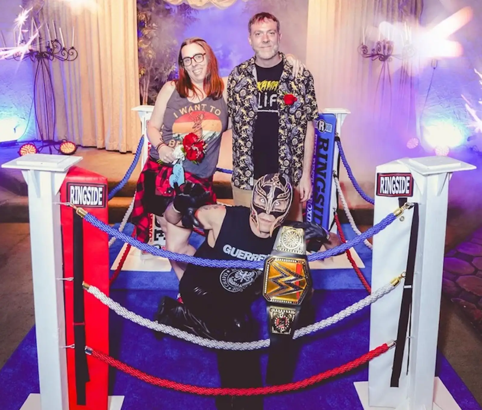 Couple posing with a masked wrestler holding a championship belt at a wrestling-themed Las Vegas wedding chapel