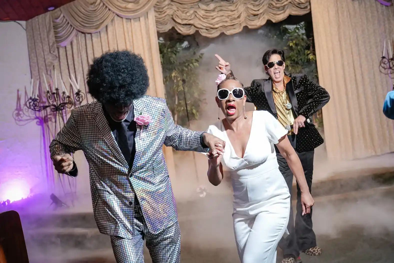 Couple dancing in disco outfits with Elvis impersonator and stage fog at a Las Vegas wedding chapel