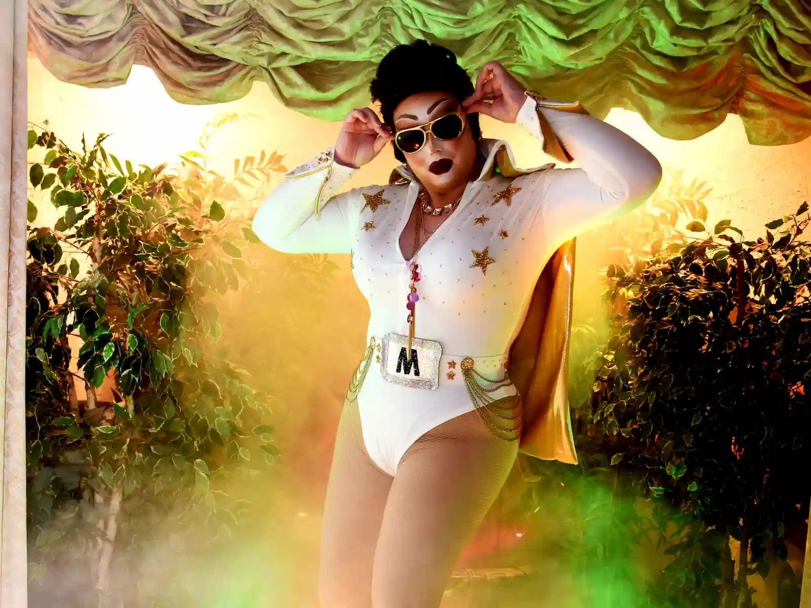 Female Elvis impersonator in white rhinestone jumpsuit with gold cape posing with dramatic fog at a Las Vegas wedding chapel