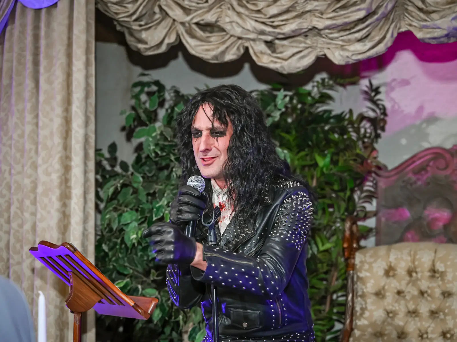 A close-up of an Alice Cooper impersonator performing into a microphone while wearing leather.