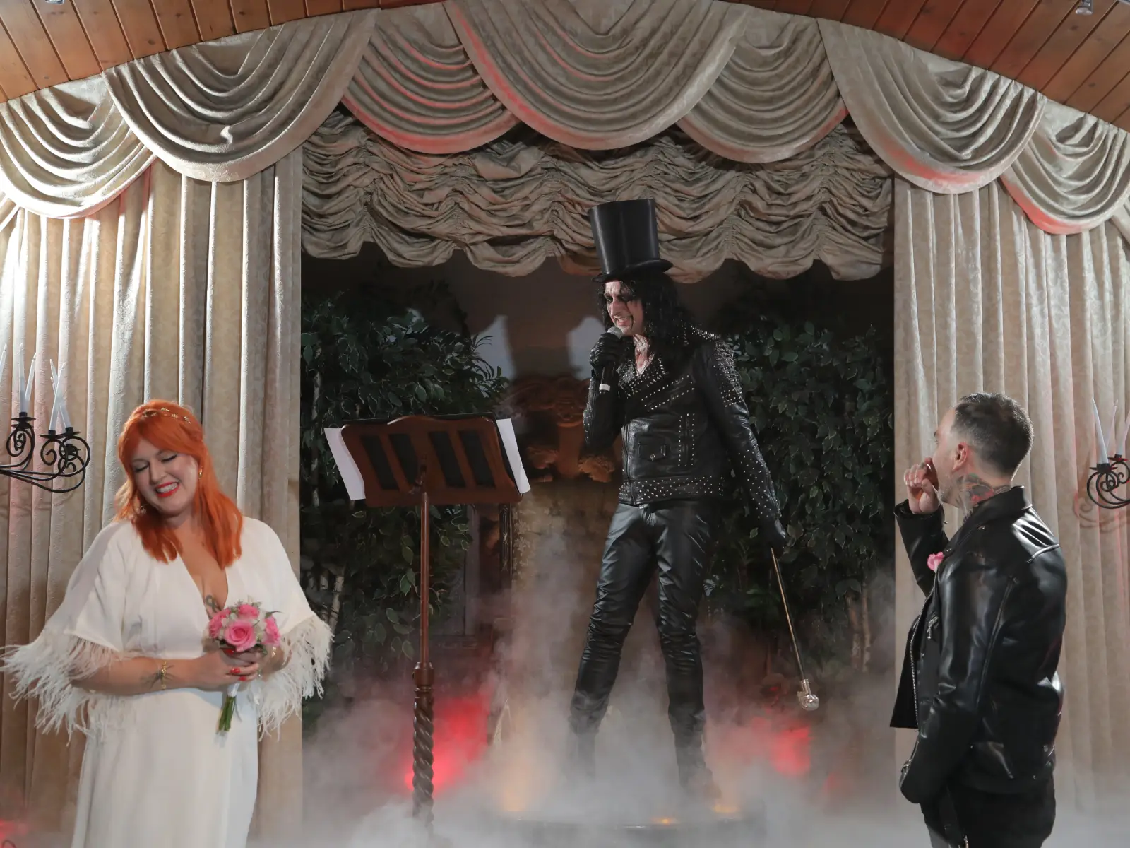 An Alice Cooper impersonator singing with a microphone and cane on stage during a wedding event.