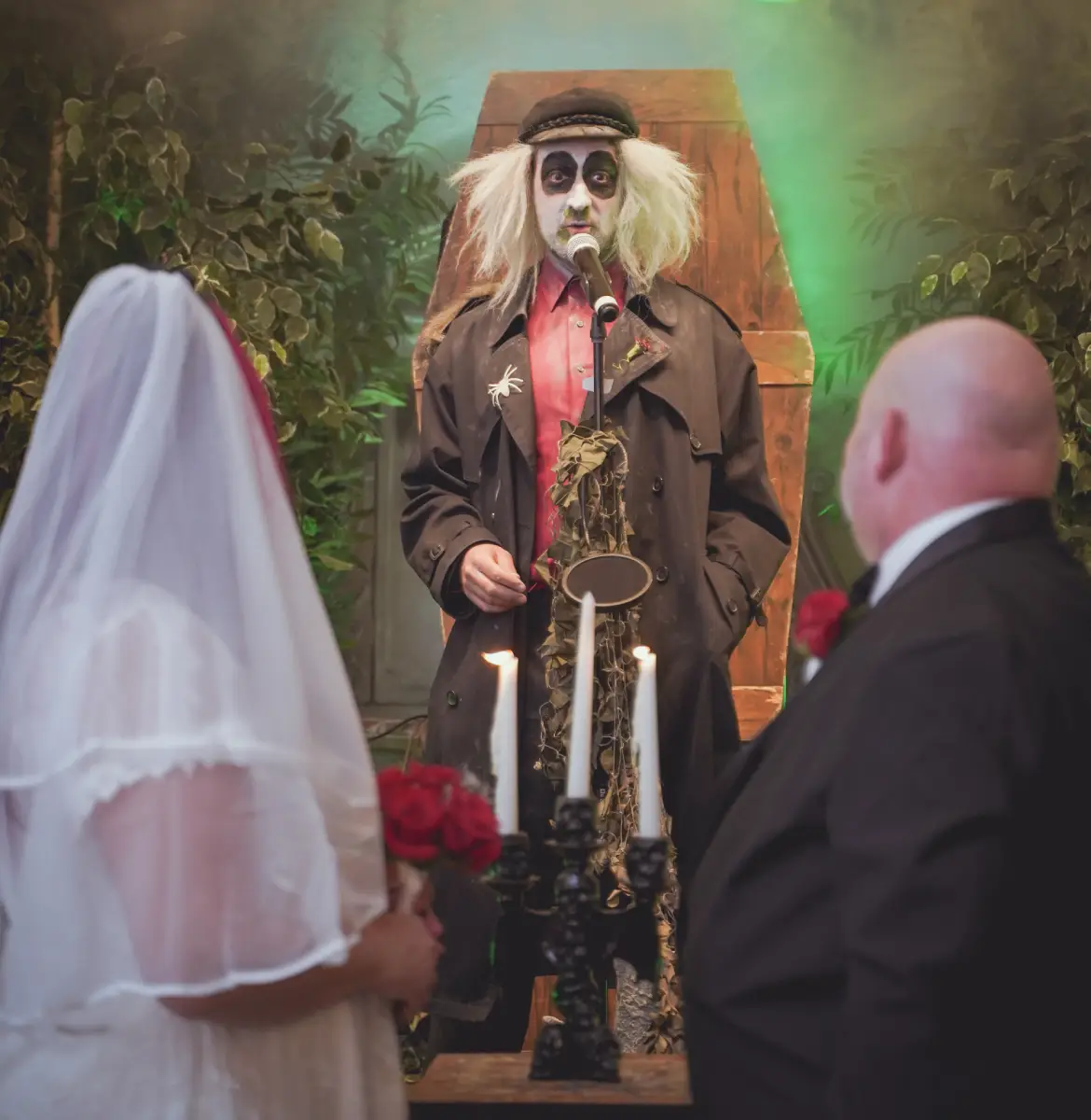 Beetlejuice-style officiant performing gothic wedding ceremony as bride and groom stand at altar with candles.