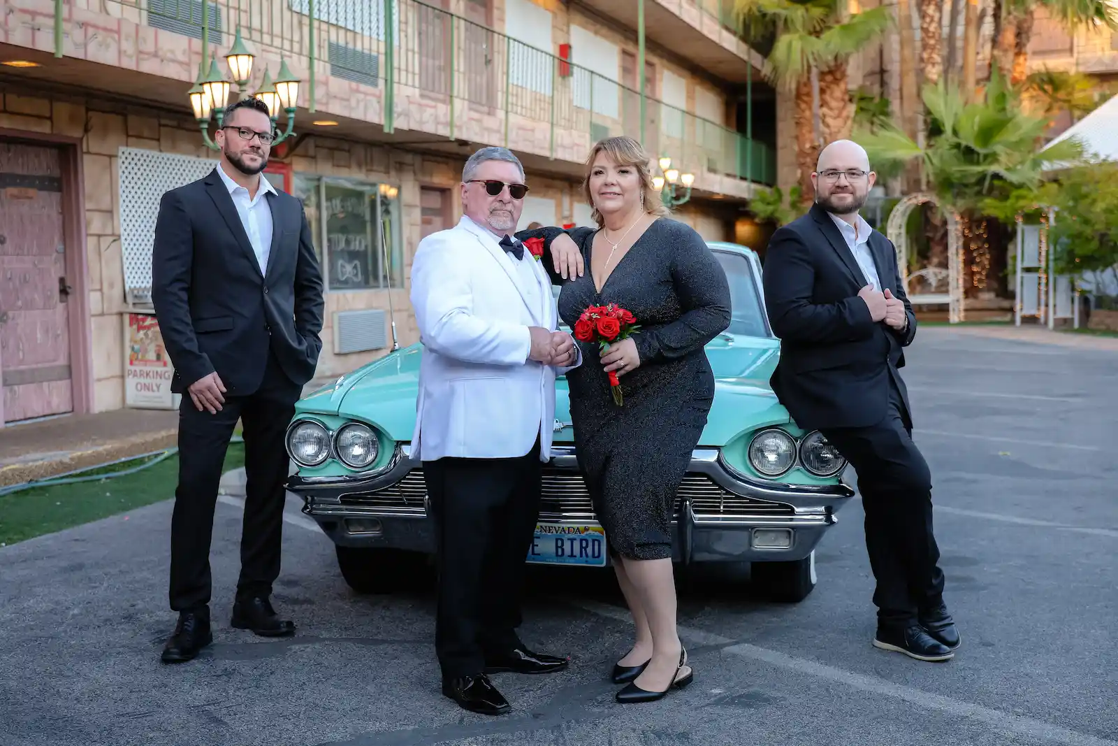 Newlyweds pose with groomsmen in front of vintage turquoise Thunderbird outside Las Vegas wedding chapel