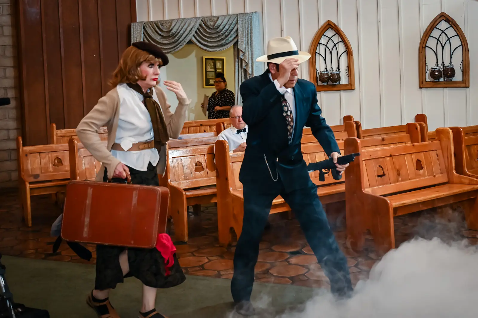 Gangster themed performers in 1920s costumes act out a dramatic scene with prop gun and suitcase in fog at Las Vegas wedding chapel