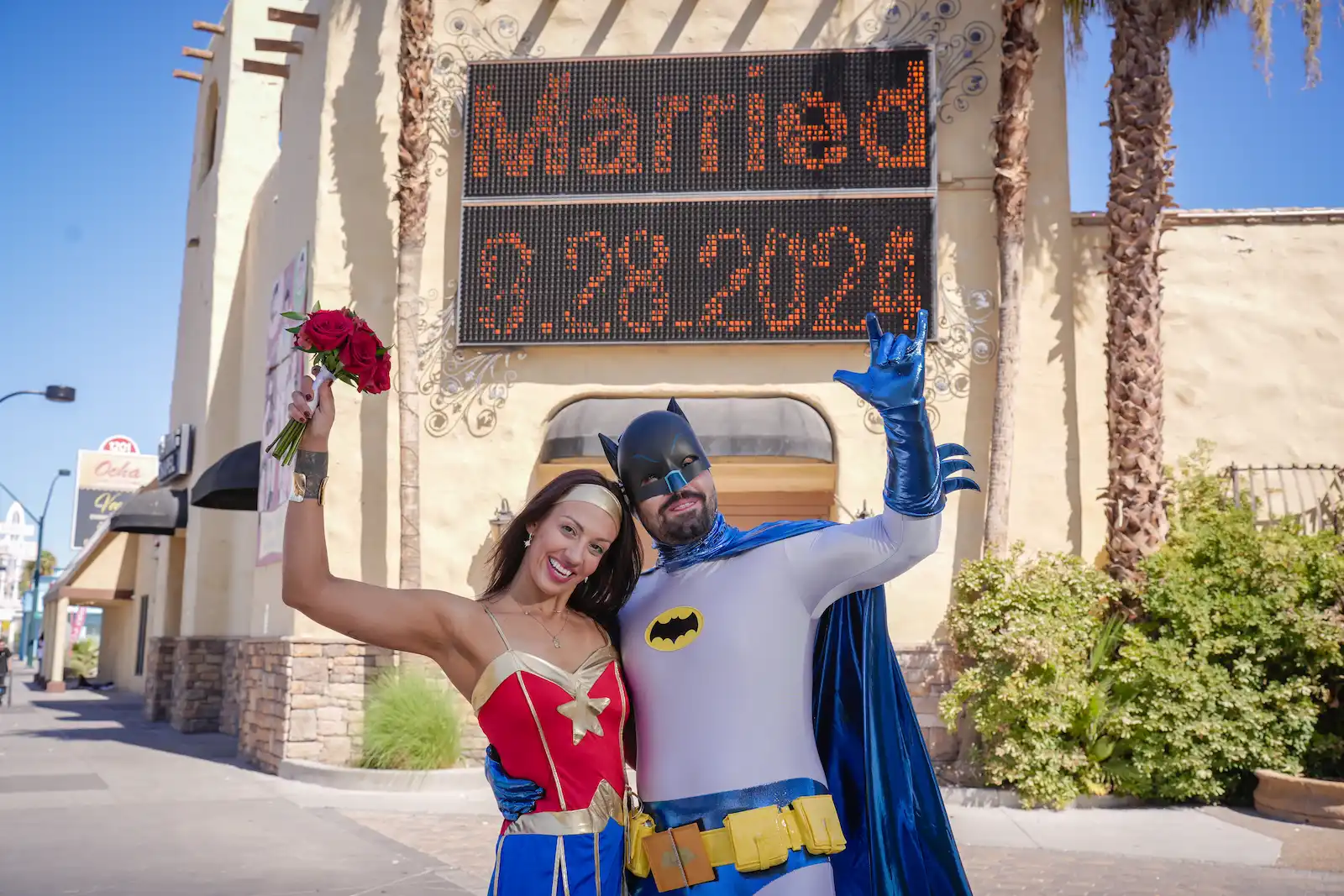 Newlywed couple in Wonder Woman and Batman costumes celebrating outside Viva Las Vegas Wedding Chapel