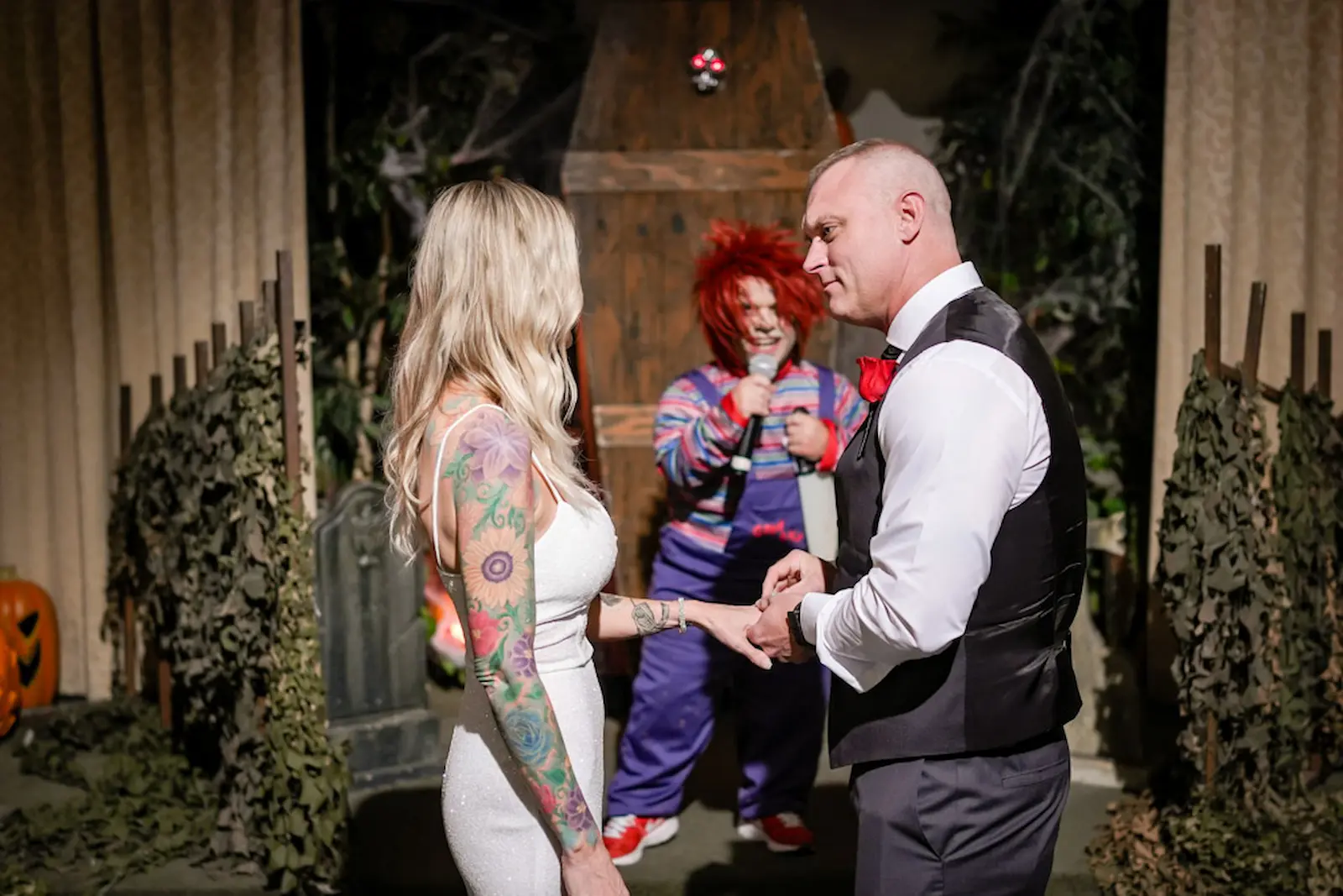 Tattooed bride and groom exchanging rings with a Chucky character officiating at a Las Vegas halloween wedding.