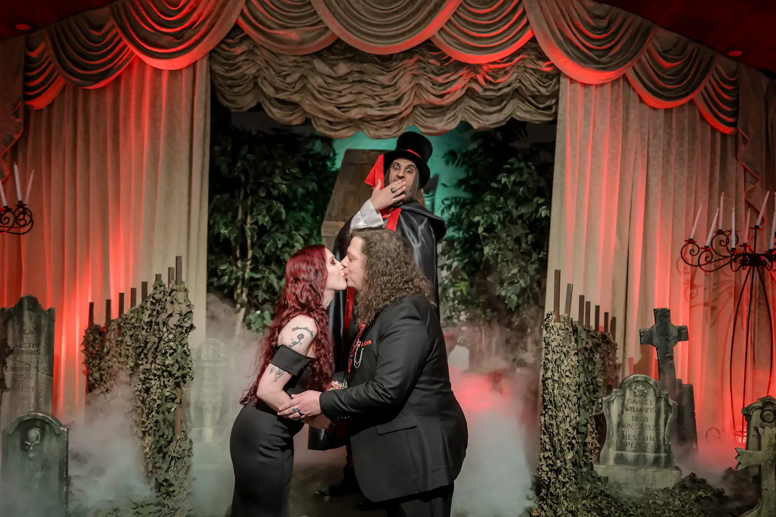 Couple sharing their first kiss in a foggy gothic graveyard while a vampire officiant reacts behind them in Las Vegas.