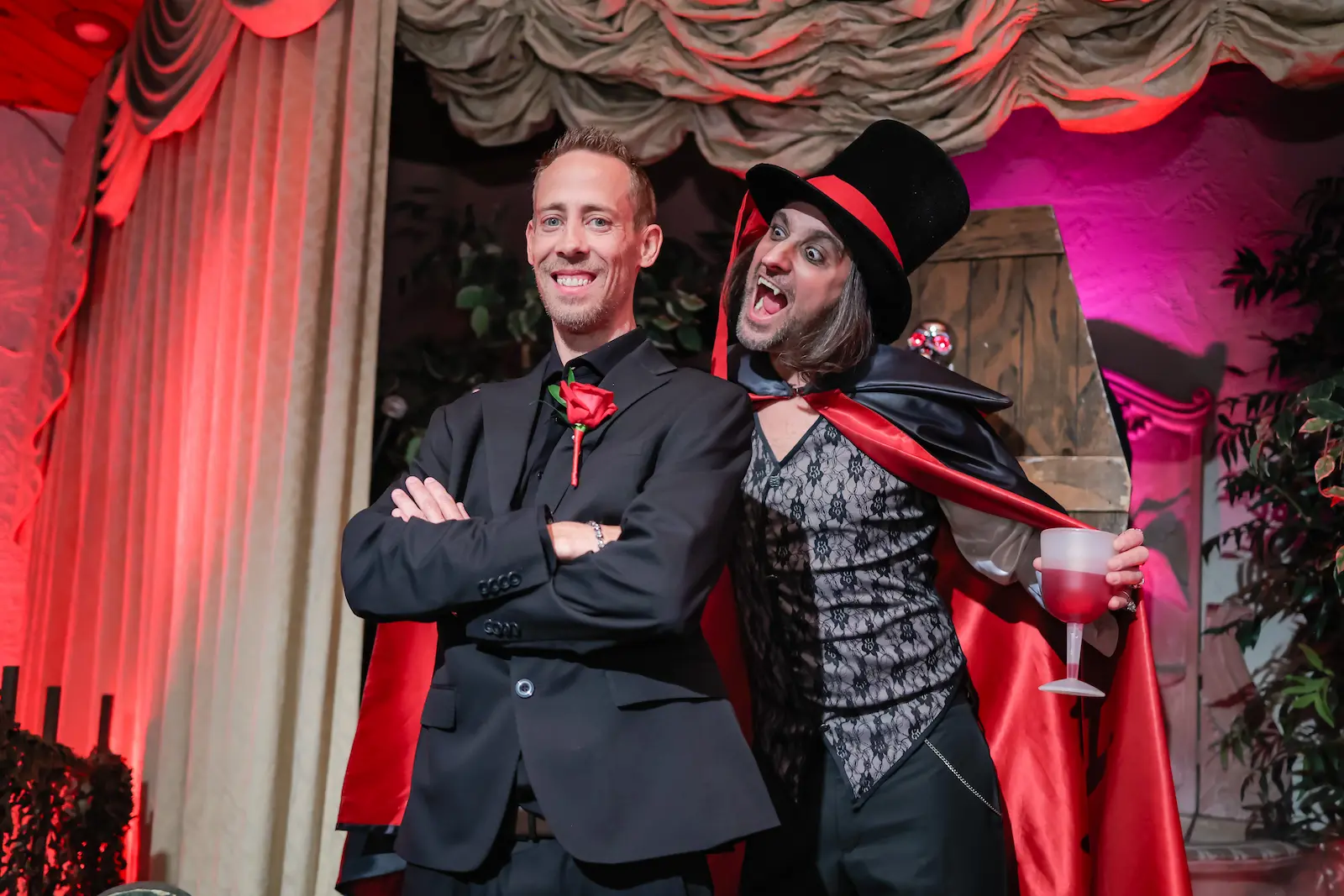 Groom posing back-to-back with a vampire officiant holding a goblet at a Las Vegas gothic wedding venue.