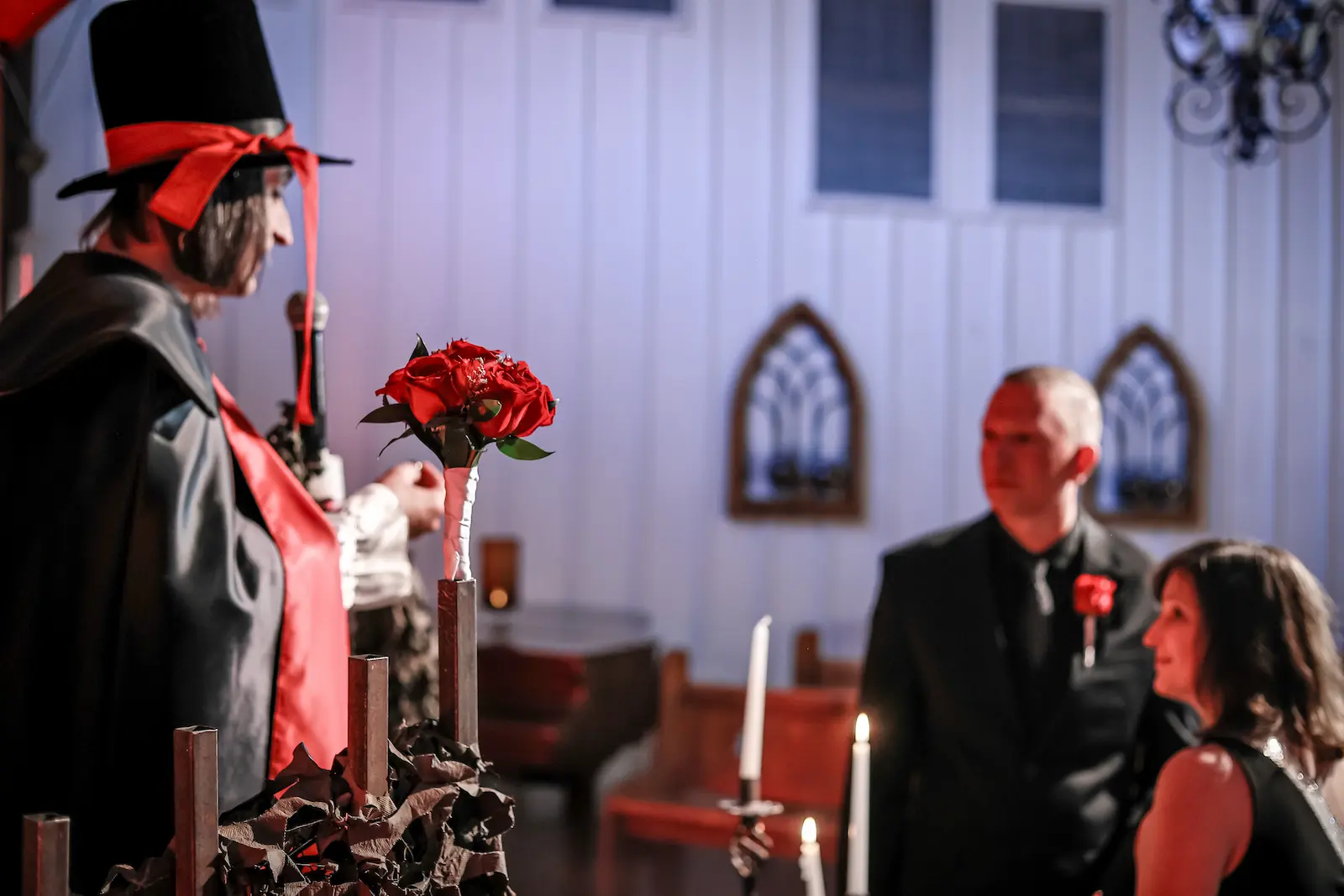 Vampire officiant holding red roses at the altar of a Las Vegas gothic wedding chapel with candles and arched windows.