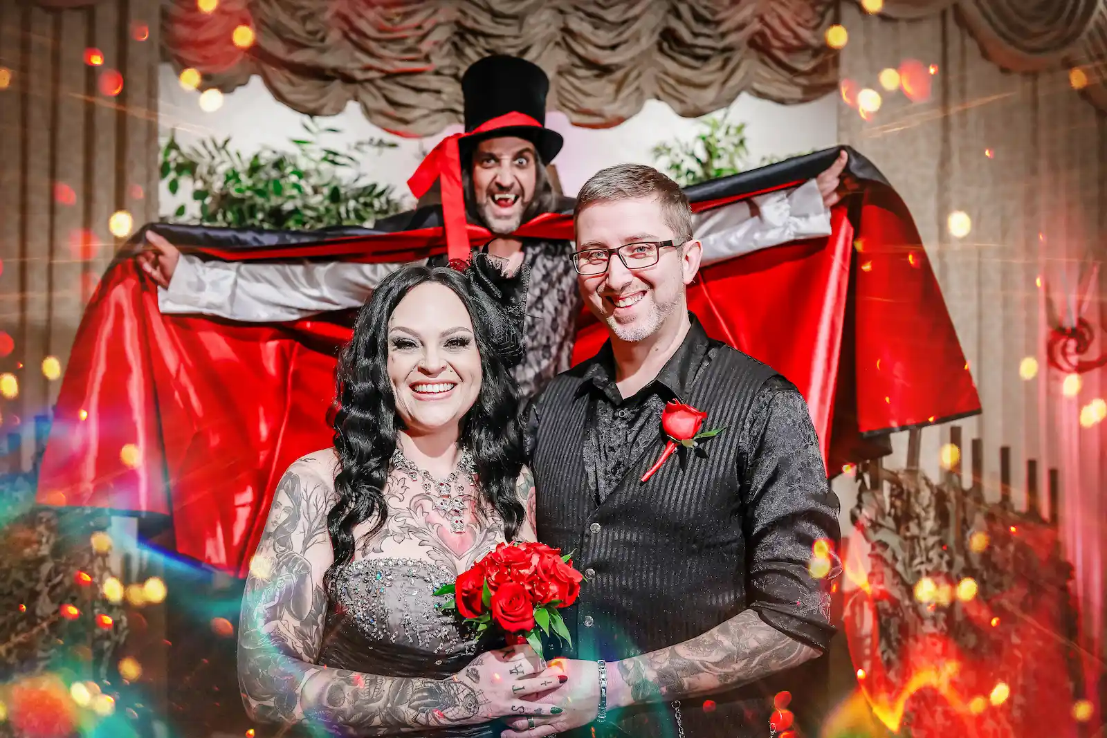Tattooed couple smiling with a vampire officiant spreading his cape behind them at a Las Vegas gothic wedding.