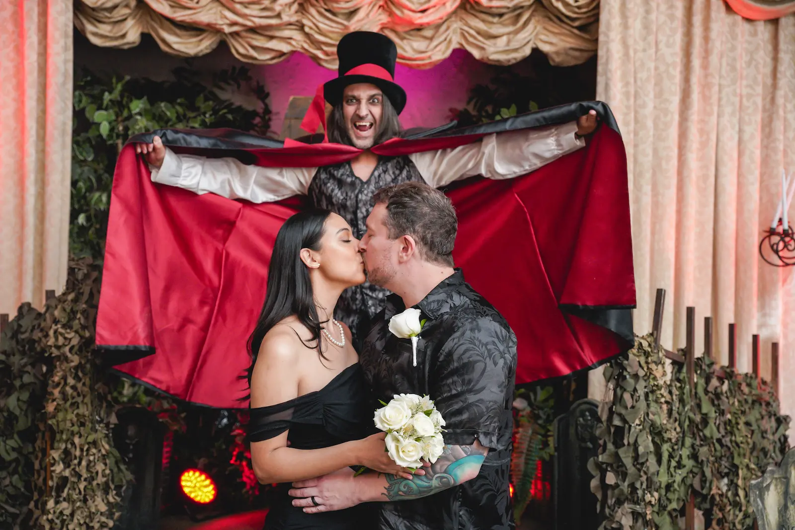 Couple sharing their first kiss as a vampire officiant spreads his cape behind them at a Las Vegas gothic wedding.