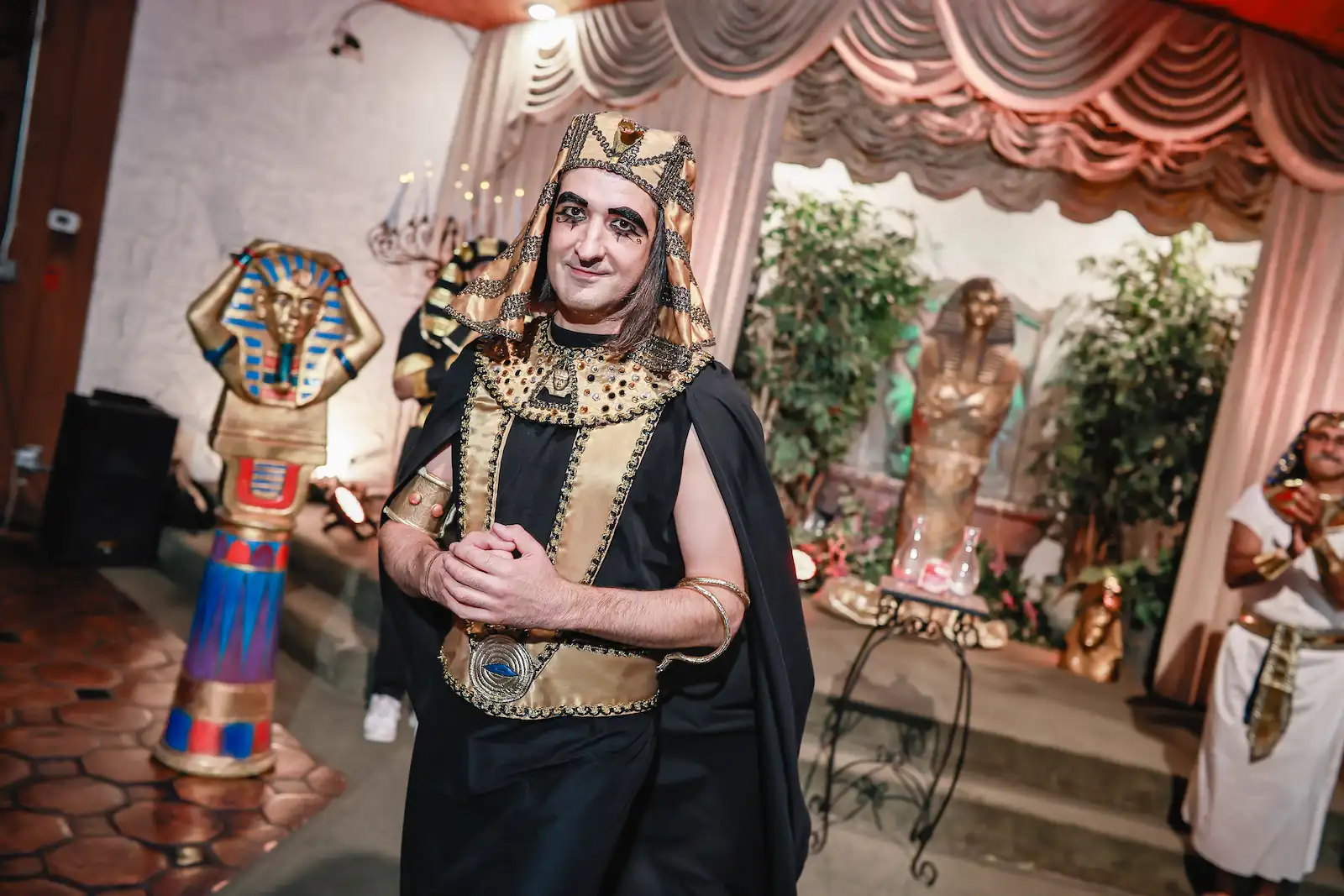 Egyptian pharaoh impersonator in gold headdress and black cape poses beside King Tut statues at Las Vegas wedding chapel