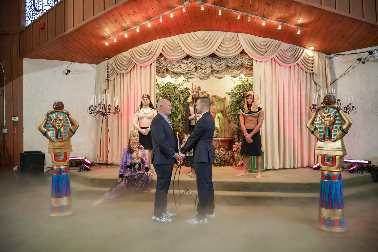 Same sex couple exchanges vows surrounded by Egyptian pharaoh officiant and performers flanked by King Tut statues at Las Vegas chapel