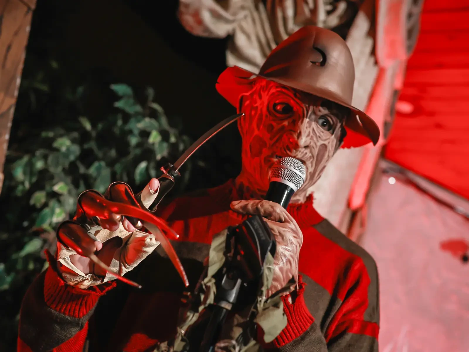 Freddy Krueger performer holding microphone and glove blades under red lighting at themed wedding.