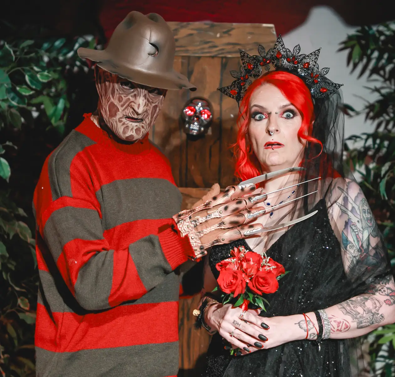 Freddy Krueger posing with bride in gothic black dress holding red bouquet at horror-themed wedding.