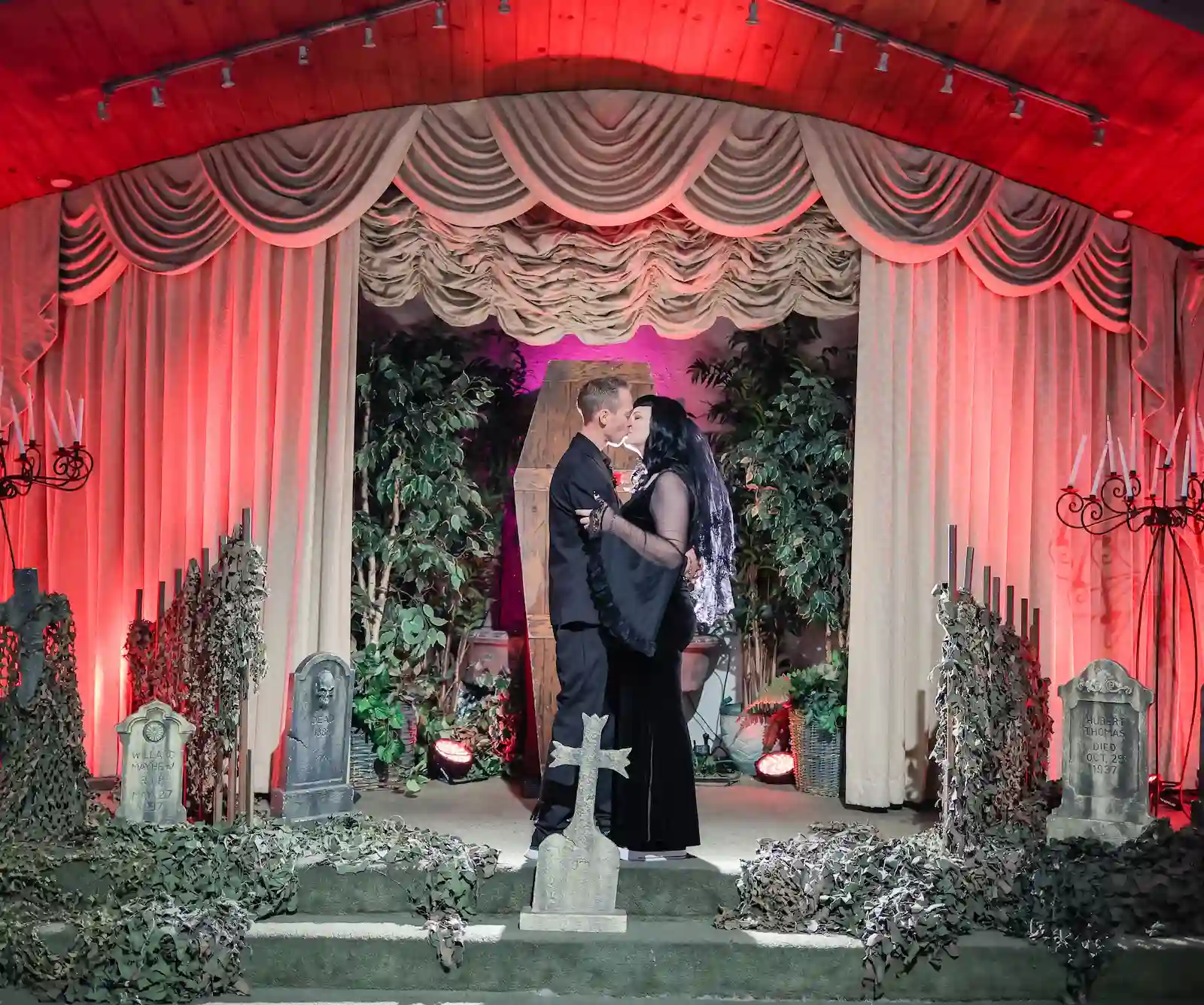 Couple sharing a first kiss during a gothic-themed wedding ceremony surrounded by tombstones and coffin backdrop at Viva Las Vegas Wedding Chapel.