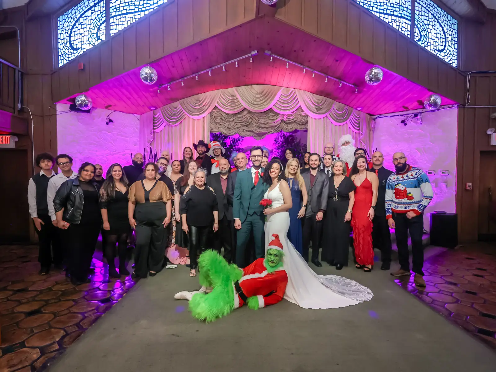 Large wedding party poses for group photo, featuring the Grinch in a Santa suit on the floor.