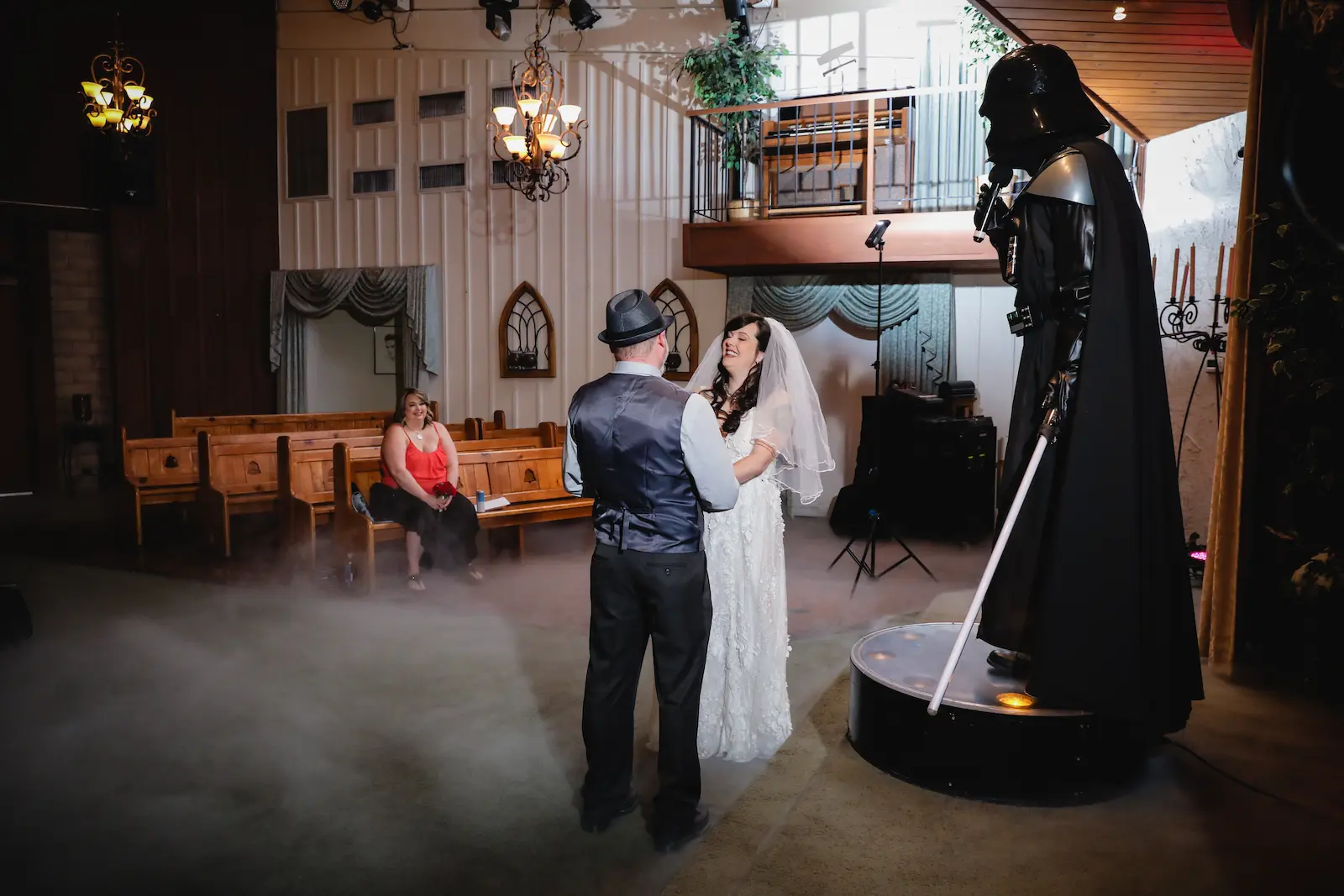 Laughing bride and groom exchanging vows in a fog-filled Las Vegas chapel with a Darth Vader character beside them.