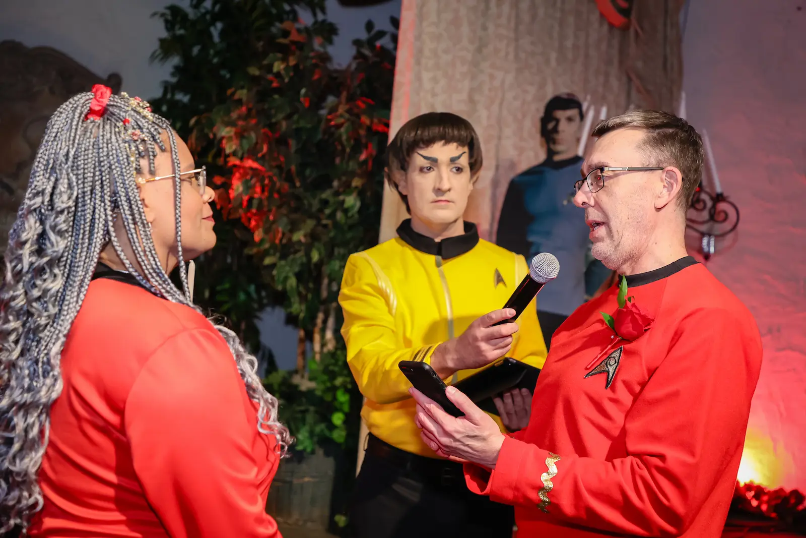 Couple in Star Trek red uniforms exchanging vows with a Spock character officiating at a Las Vegas intergalactic wedding.