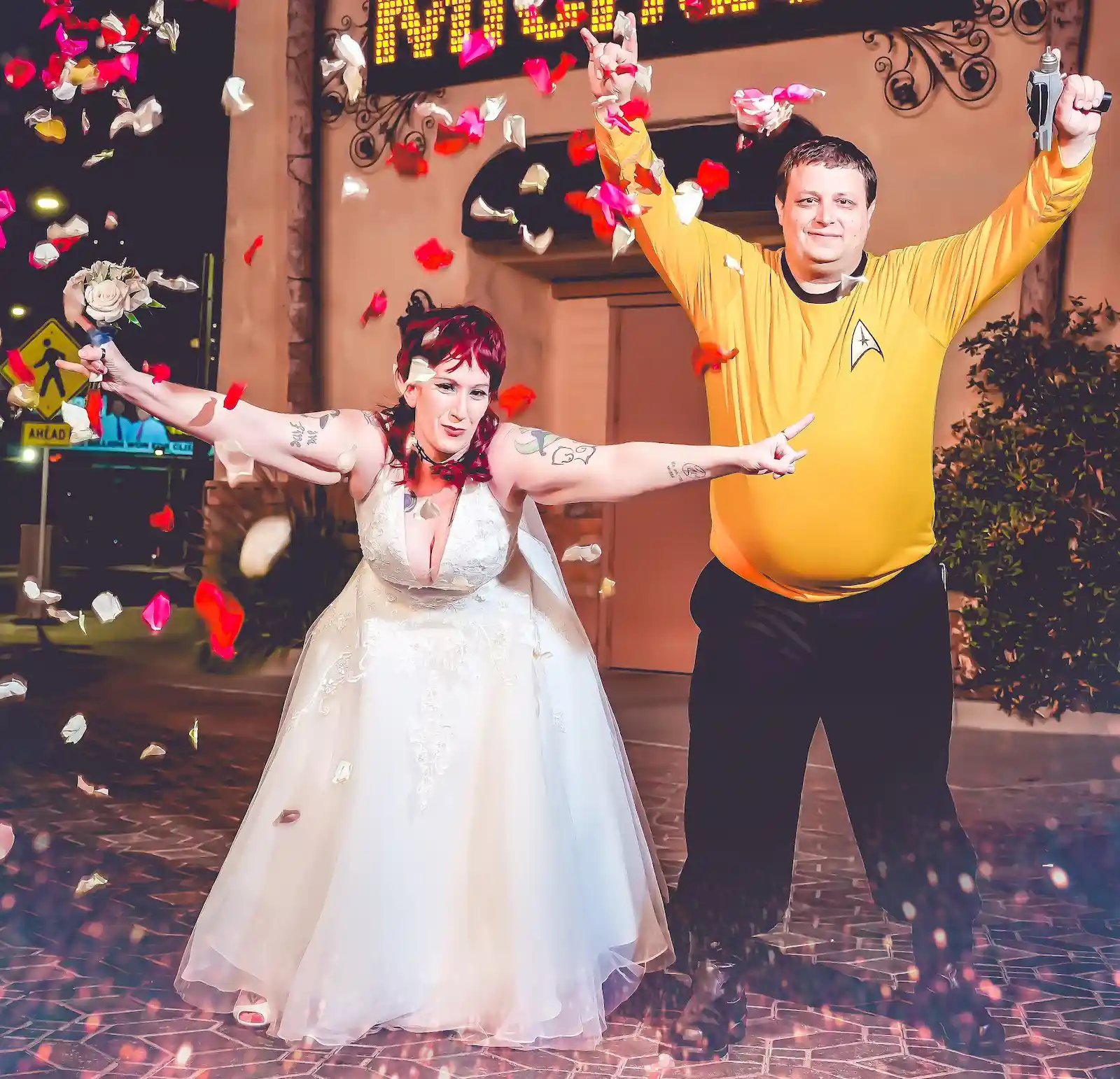 Star Trek-themed couple celebrating with arms raised as rose petals fall around them outside a Las Vegas wedding chapel.