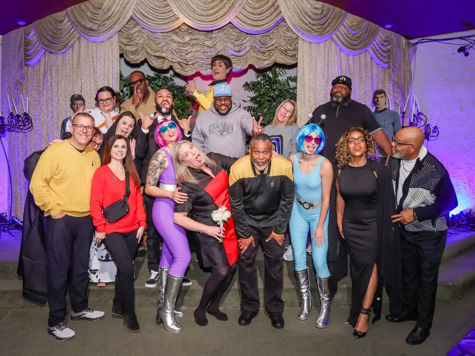 Wedding guests in Star Trek-themed costumes posing for a group photo in front of a curtained backdrop