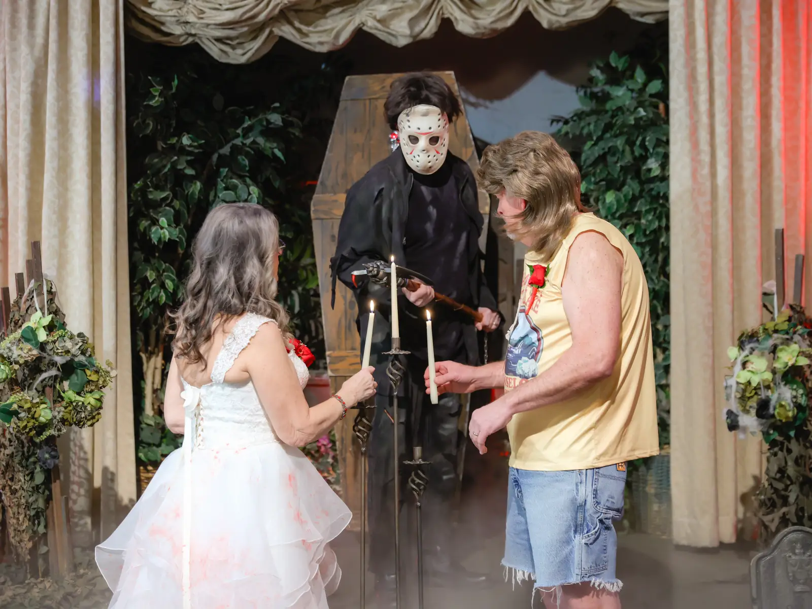 Couple holds candles during a spooky Las Vegas wedding ceremony with a masked officiant, fog, and cemetery-style decor.