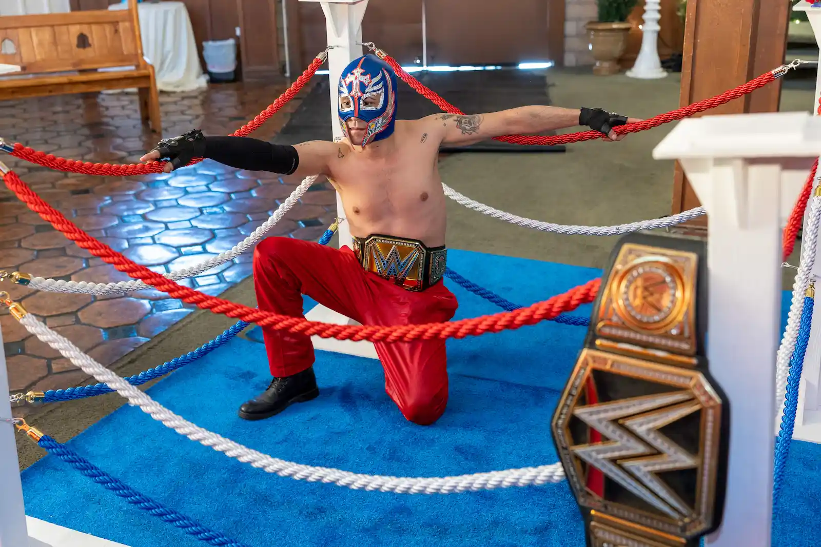 Luchador wrestler in blue mask and championship belt kneels dramatically in wrestling ring at Las Vegas wedding chapel