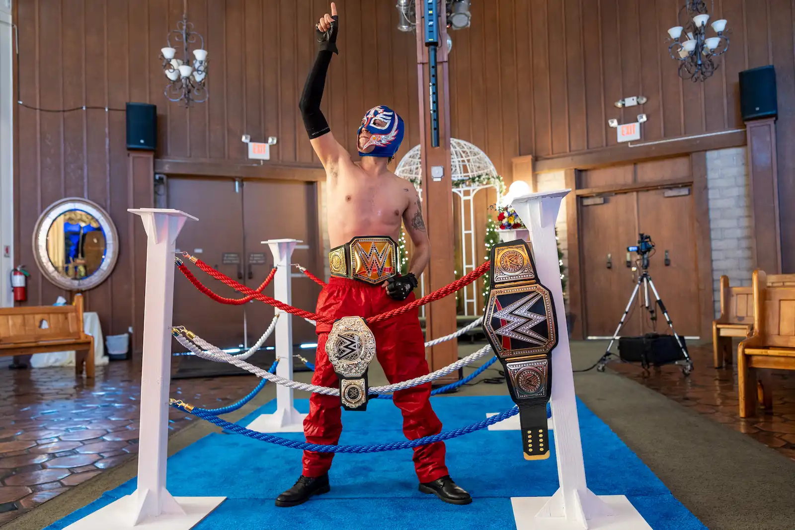 Luchador performer in blue mask raises fist while wearing championship belt inside wrestling ring at Las Vegas wedding chapel