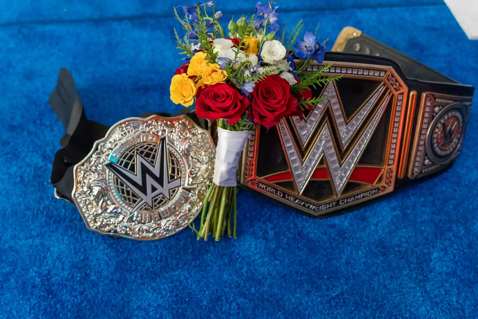 Wedding bouquet rests between two WWE championship belts on blue wrestling ring mat at Las Vegas chapel