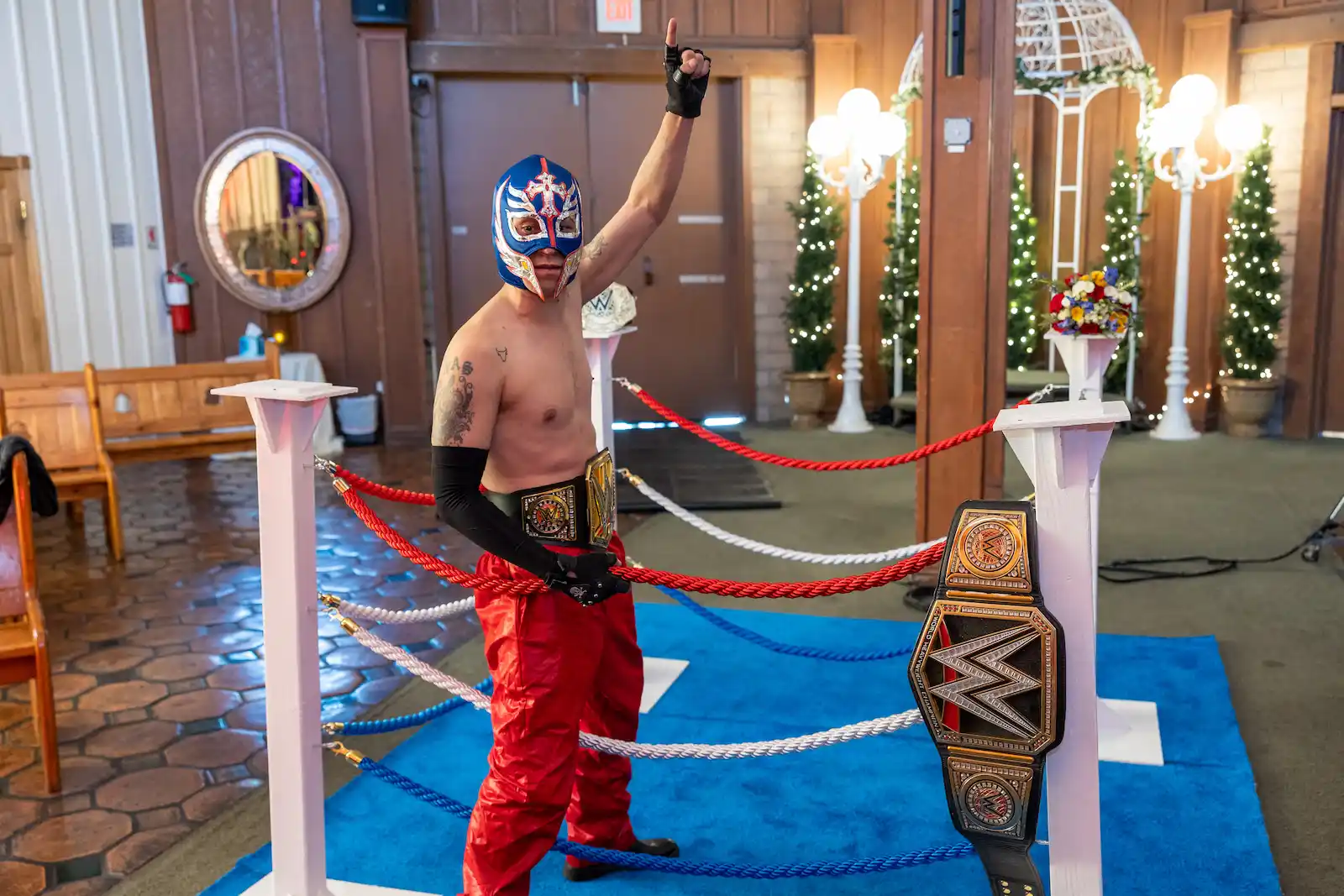 Masked luchador wrestler gives thumbs up beside championship belt in wedding chapel wrestling ring in Las Vegas