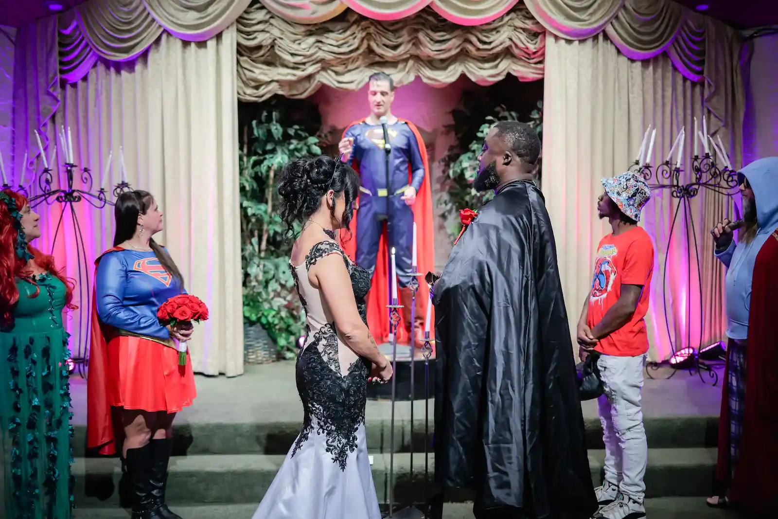 Couple in superhero costumes exchange vows as Superman officiant performs ceremony surrounded by cosplay guests at Las Vegas wedding chapel