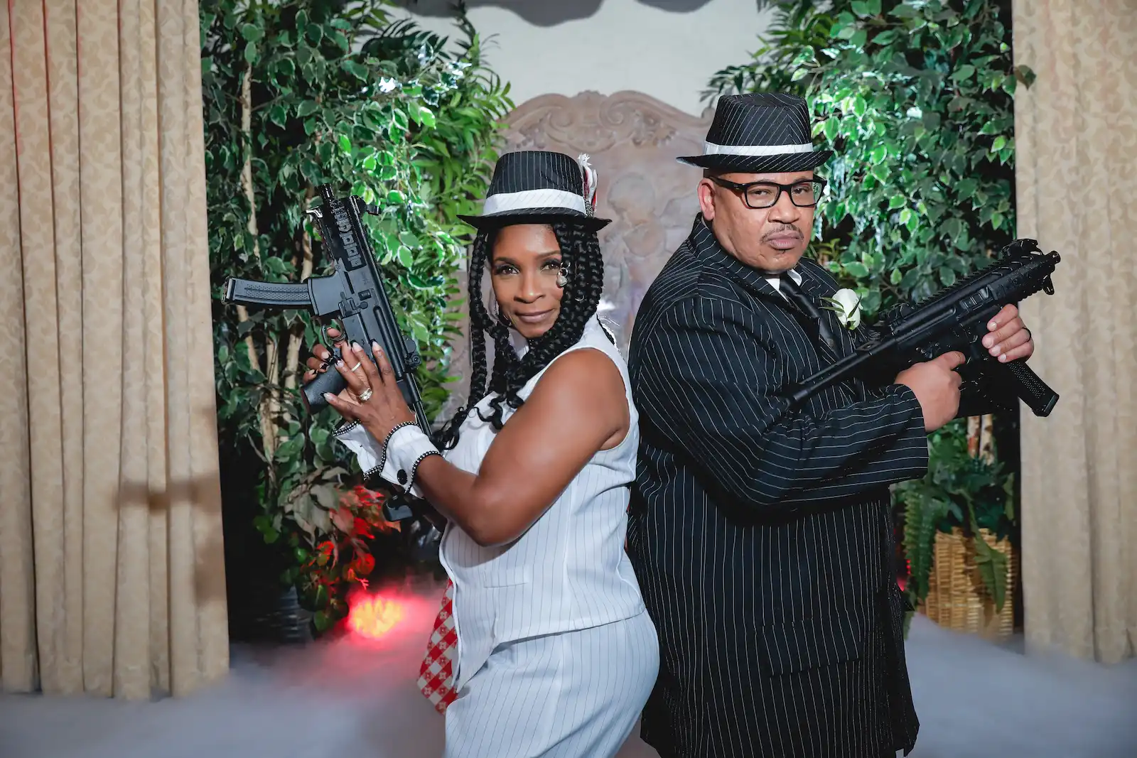Newlyweds in matching pinstripe gangster outfits pose back to back with prop guns at Las Vegas wedding chapel