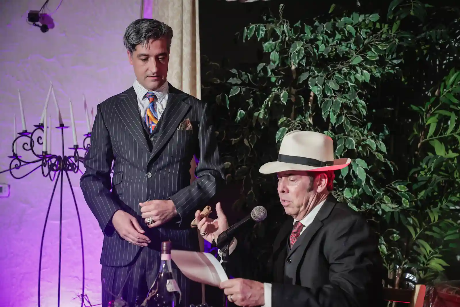 Groom in pinstripe suit stands beside Godfather impersonator reading ceremony script at Las Vegas wedding