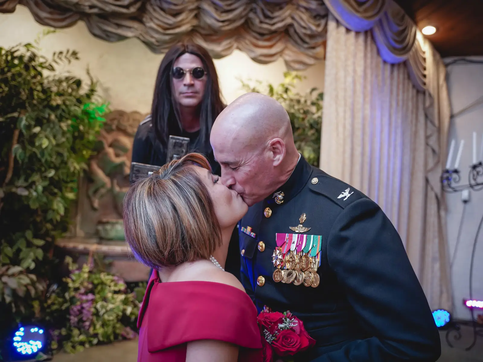 Military groom kisses bride in a red dress during a gothic themed Las Vegas wedding ceremony.