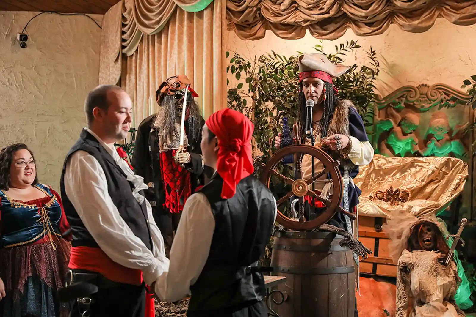 Costumed wedding party gathered around a ship wheel during a pirate-themed ceremony at a Las Vegas wedding chapel.