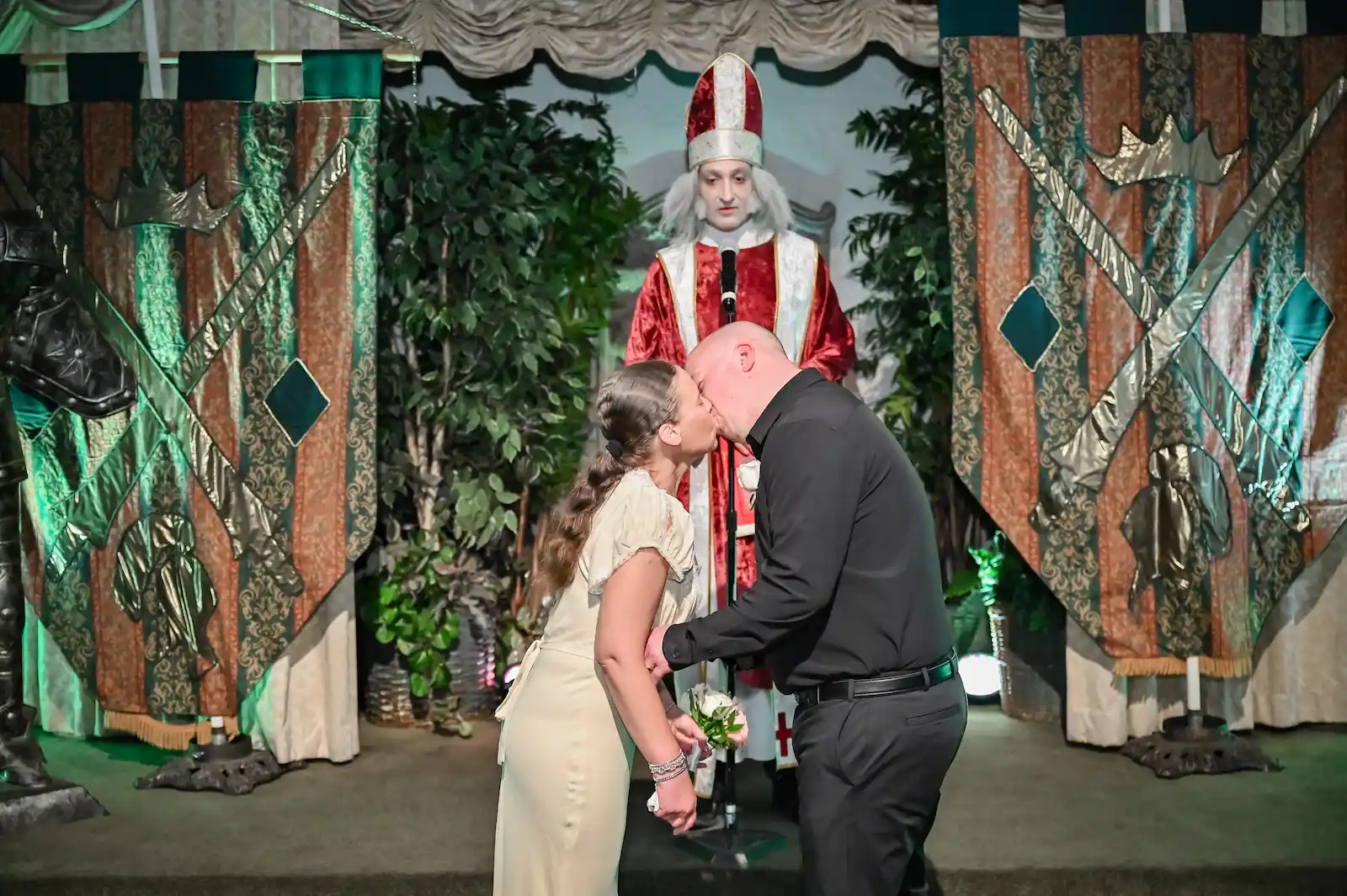 Couple sharing their first kiss before a medieval bishop officiant with royal banners at a Las Vegas Camelot wedding.