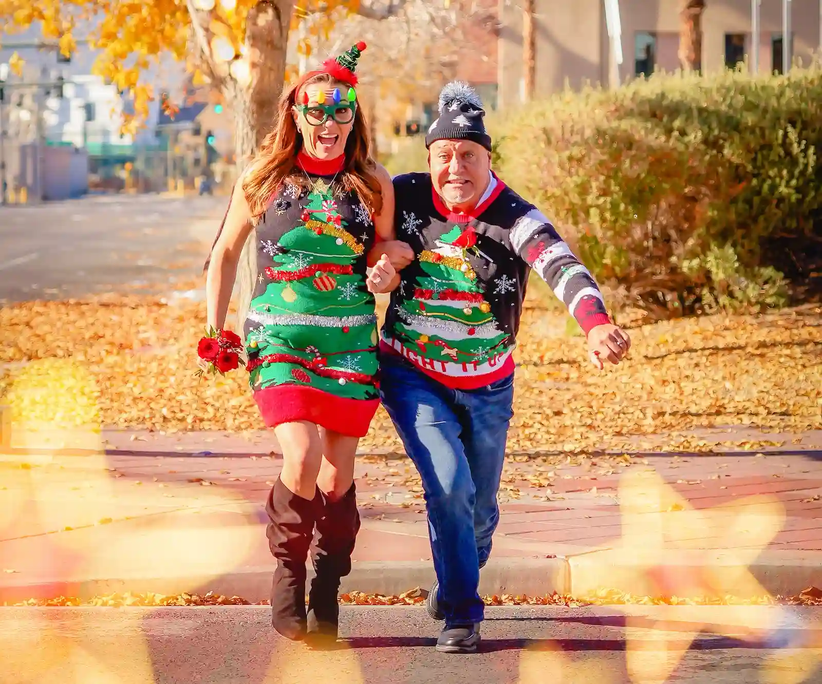 Newlywed couple in matching ugly Christmas tree sweaters run and laugh together outside Las Vegas wedding chapel