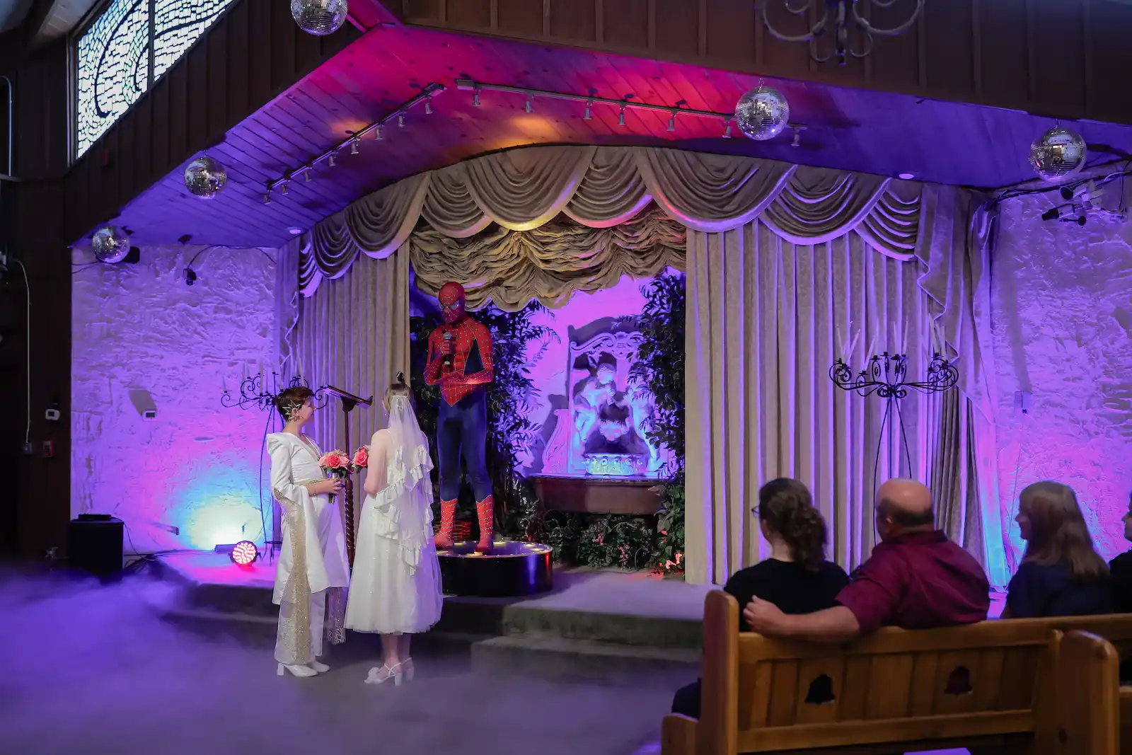 Spider-Man costumed officiant presides over same sex wedding ceremony under purple lighting at Las Vegas chapel